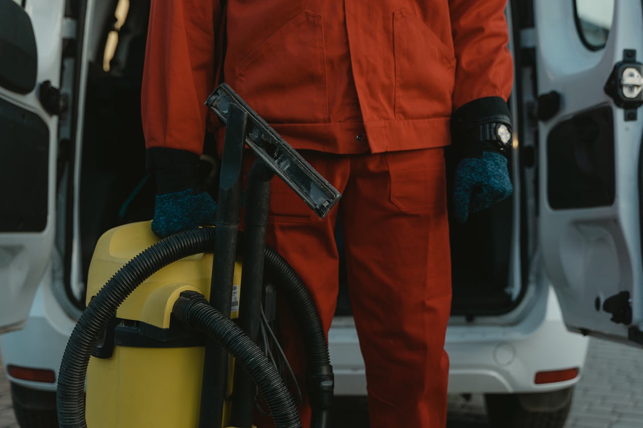 services-04 A professional cleaner in a red uniform holding a vacuum near a van, ready for service.